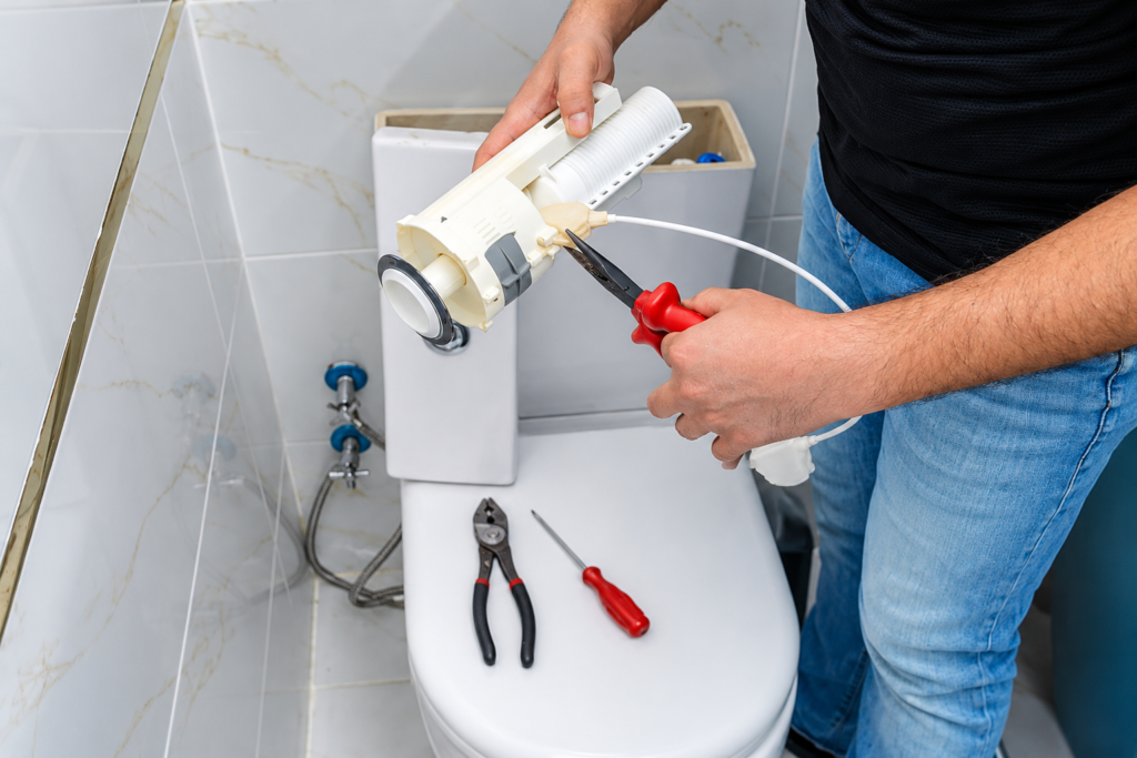 Plumber replacing a toilet flush valve mechanism with hand tools.