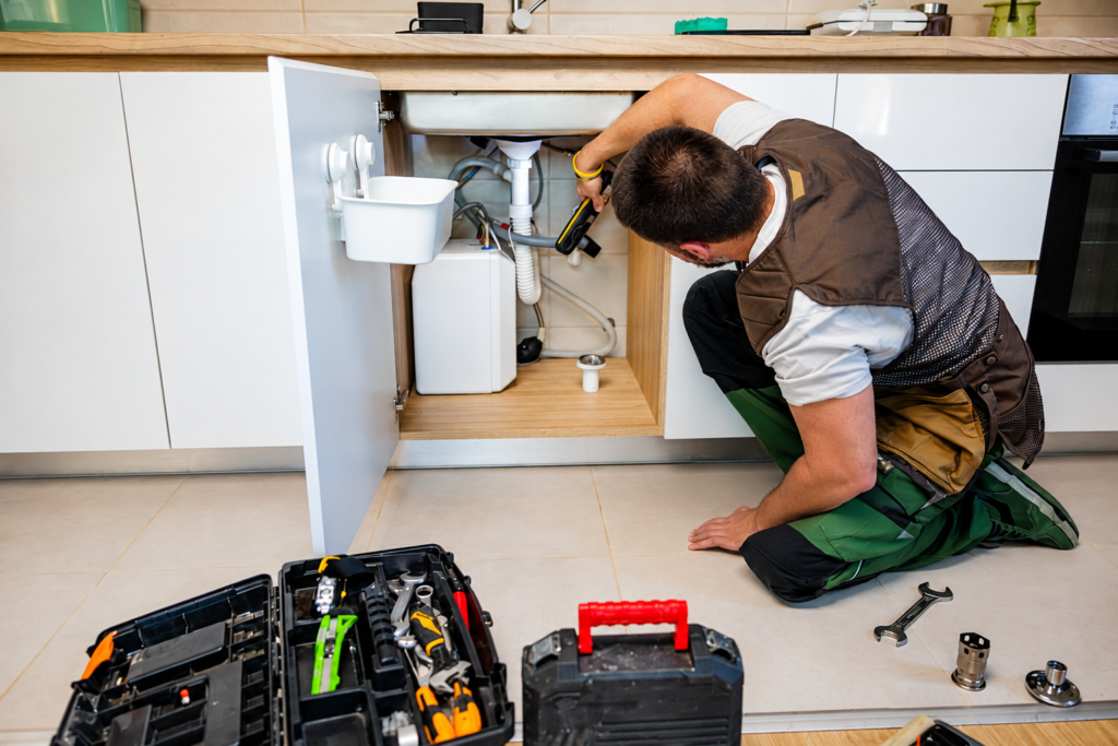 Plumber inspecting and repairing under-sink plumbing in a modern kitchen.